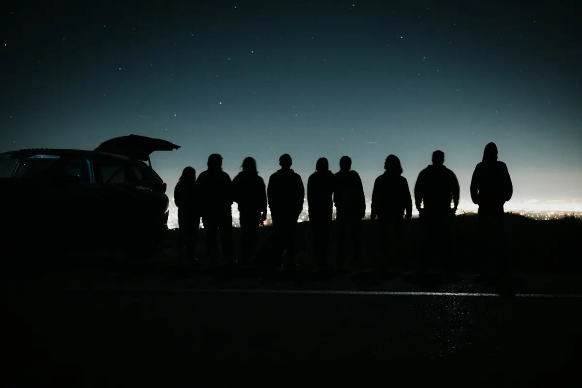 A line of friends silhouetted next to a car at dusk