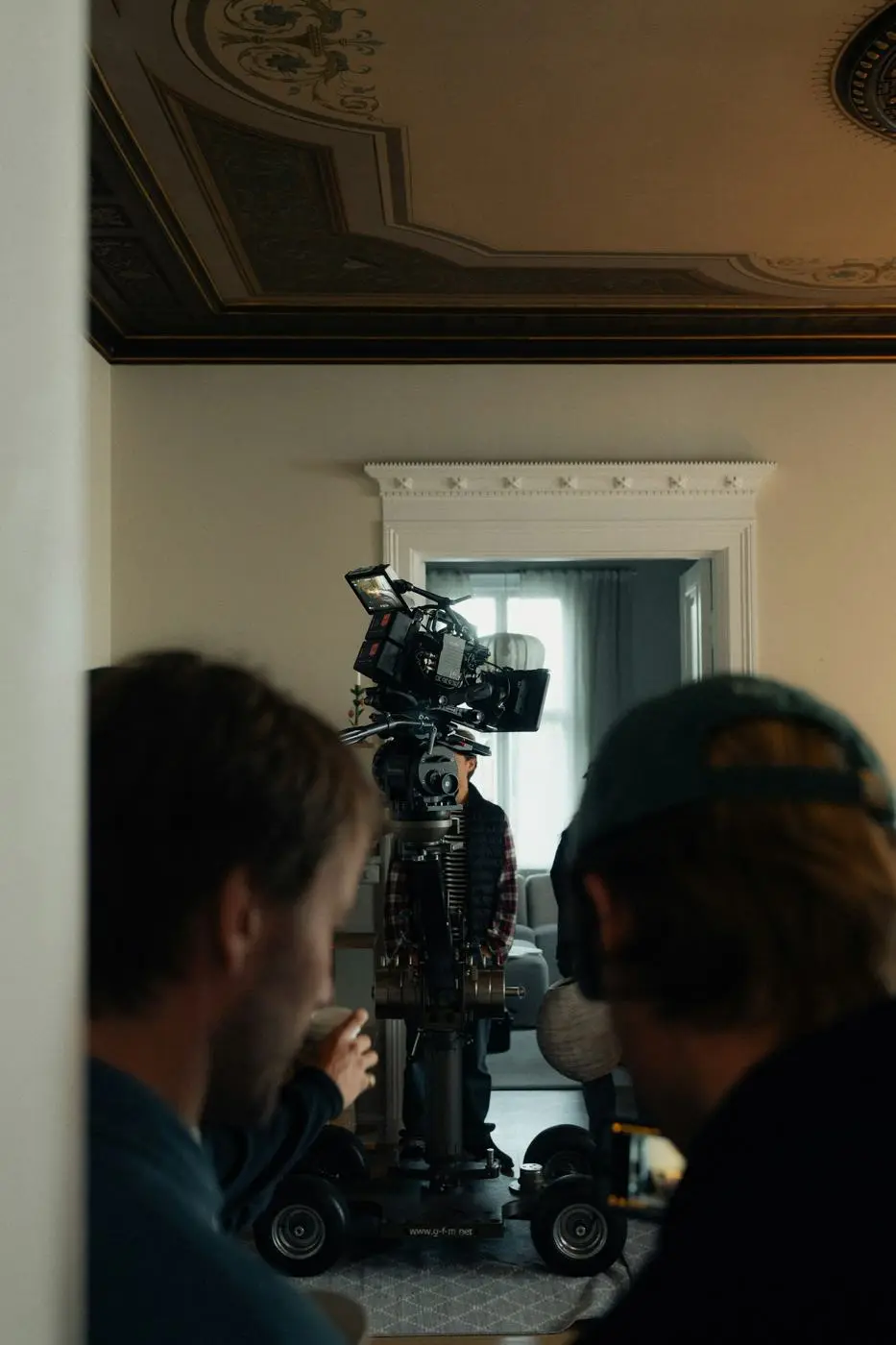 Two crew members by a camera on a dolly in a doorway