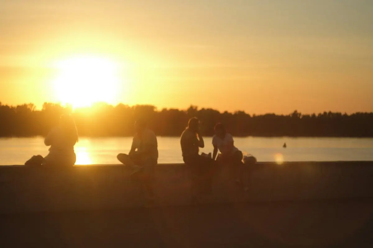 Friends sitting on a wall by the water as the sun goes down