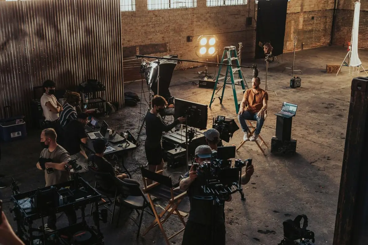 A small crew setting up around a camera in a warehouse studio