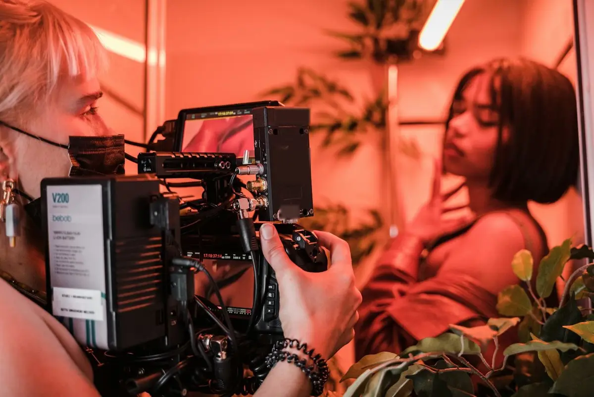 A camera operator in an orange shirt framing an actor in red light