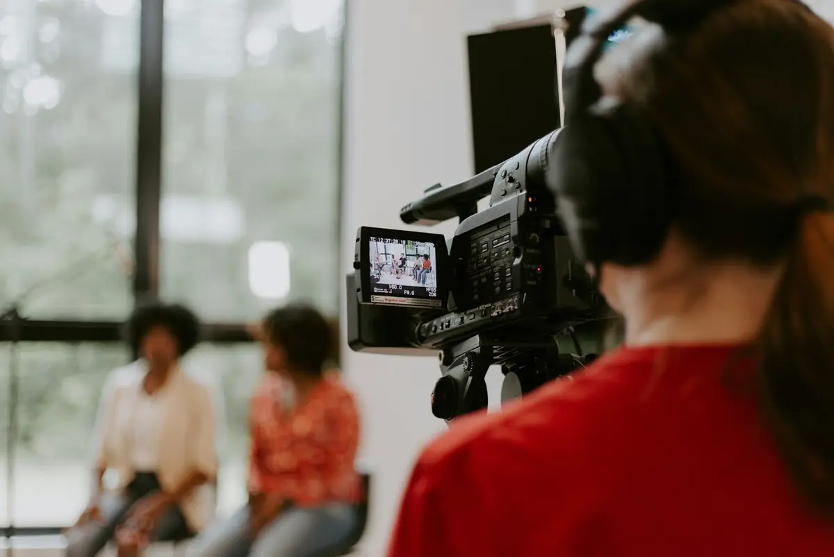 A camera operator filming two people on a sofa