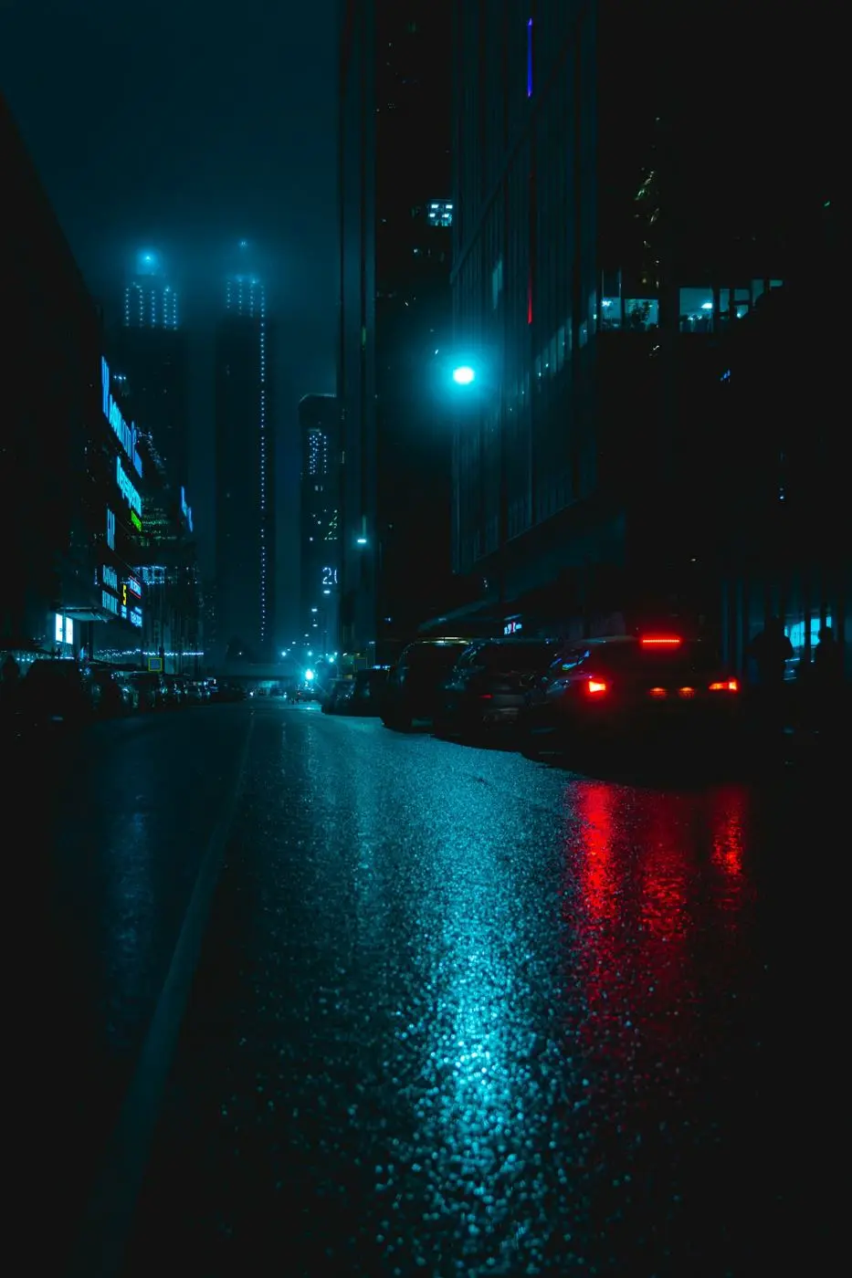 A wet city street at night, teal and red light on the road