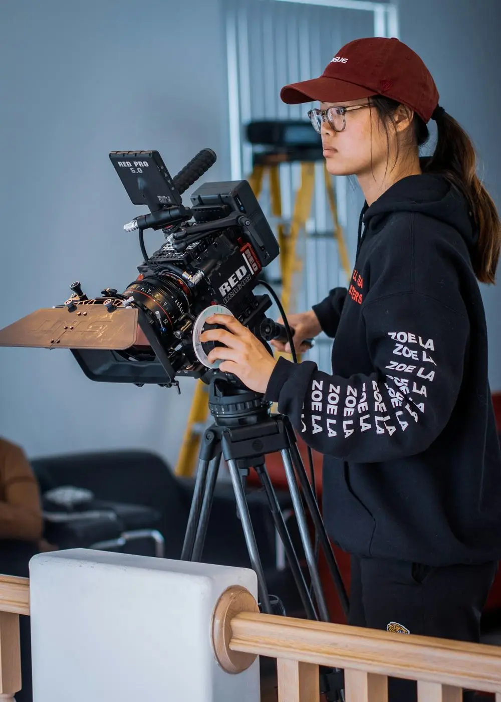 A young camera operator in a red cap setting up at a tripod